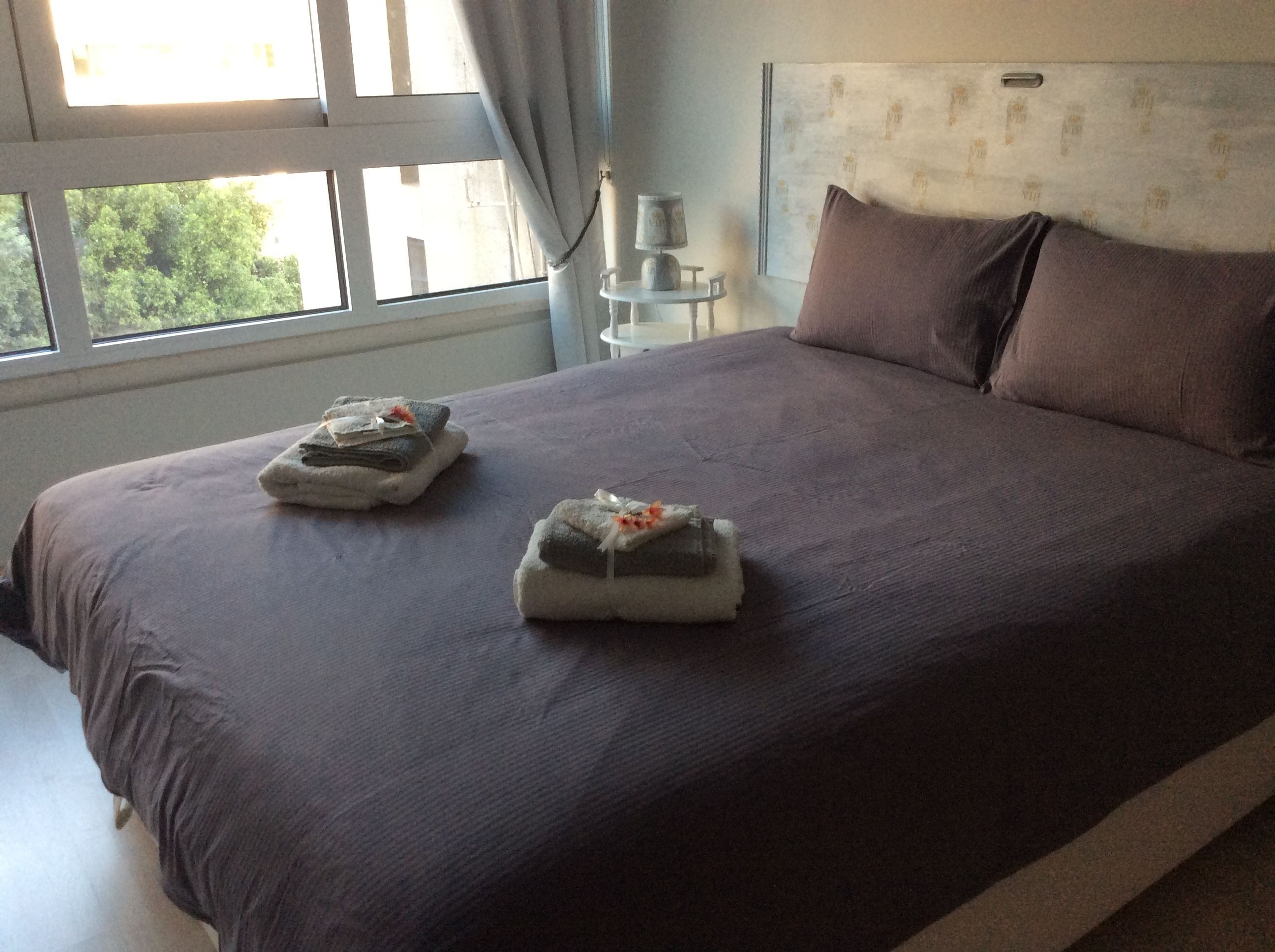 Un letto rifatto con cura, con una coperta scura e due asciugamani decorati con fiori.