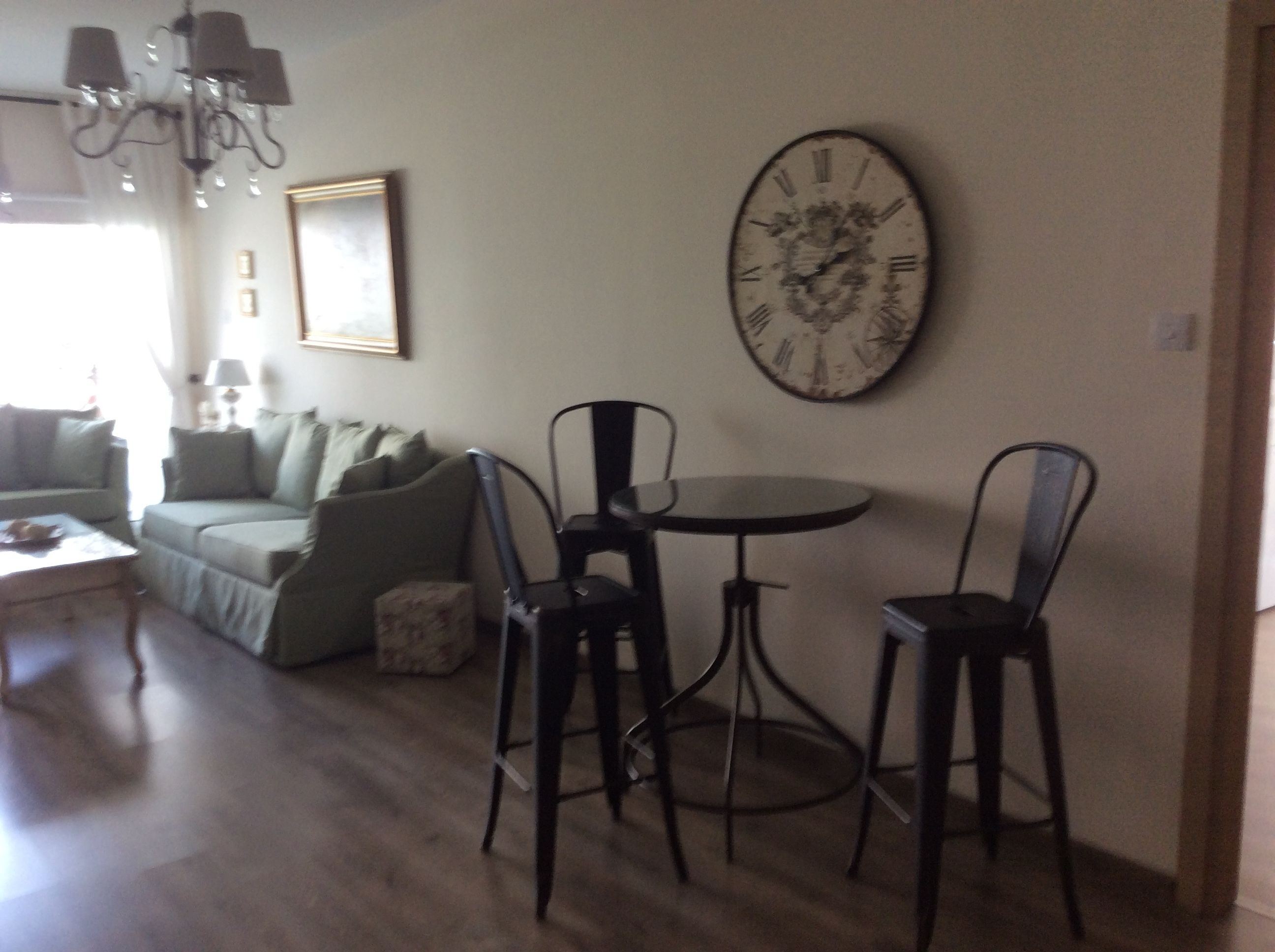 A living room with a sofa, a small table, two chairs, a round table, and a wall clock.
