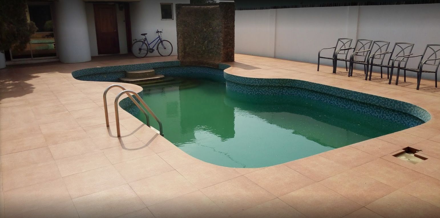 A swimming pool with a tiled deck, a metal ladder, and a few chairs.