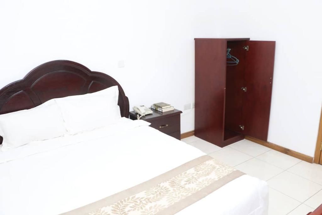 Una cama bien hecha con cubrecama blanco y beige, un cabecero de madera, una mesita de noche con teléfono y un armario con espejo.