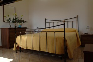 Una cama individual con estructura metálica y colcha amarilla en una habitación con un aparador de madera y un espejo en la pared.