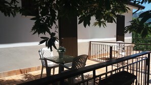 Un balcón con una mesa y sillas, una planta en maceta y vistas a la calle y montañas.