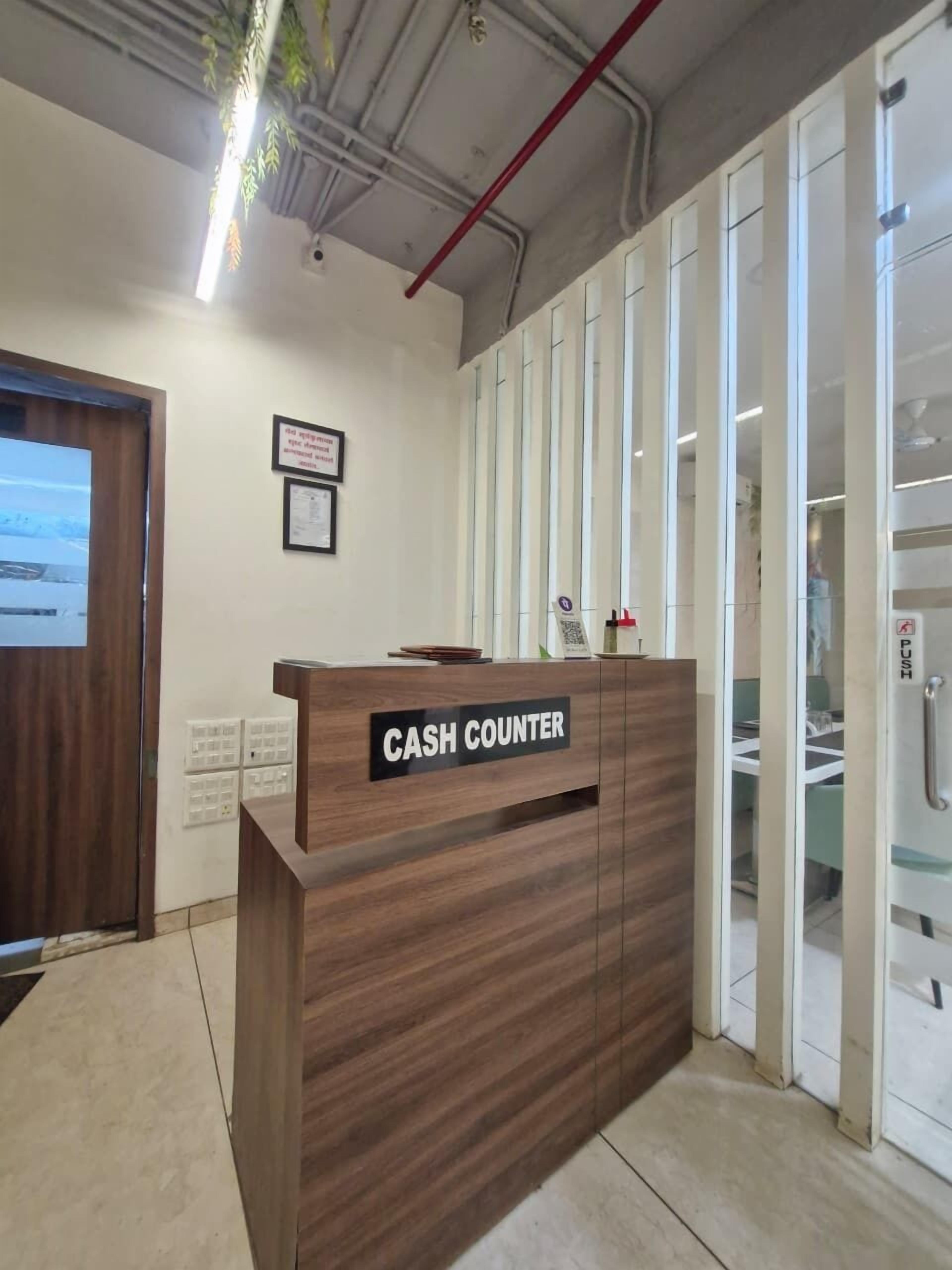 A reception desk labeled "CASH COUNTER" with a wooden finish, a framed certificate on the wall, and a glass door to the right.