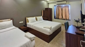 A hotel room with two beds, a desk, a ceiling fan, and a window with curtains. - Visawa Palace Nanded (Nanded)