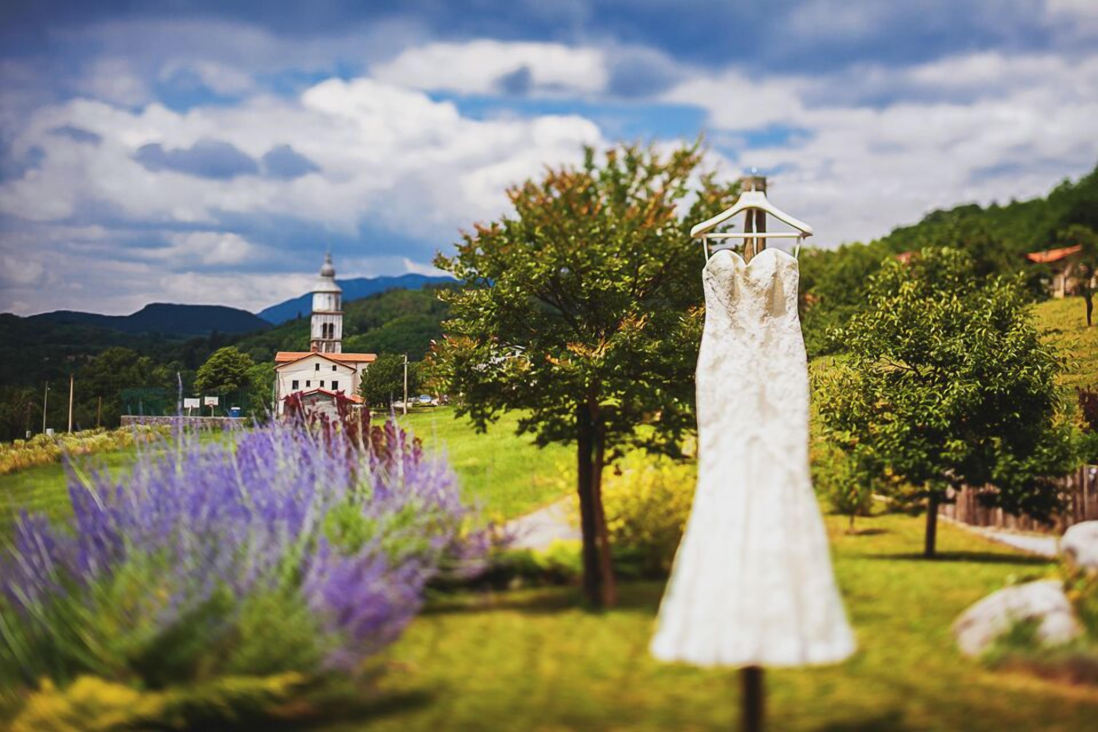 Um vestido de noiva em ambiente rural, com uma igreja e montanhas ao fundo.