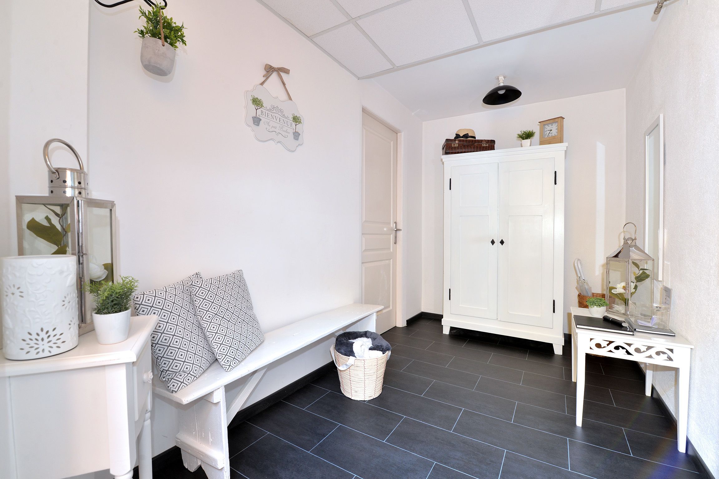 A clean, white interior with a bench, a white cabinet, and a small table with a plant.