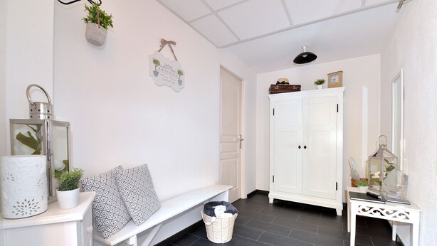 A clean, white interior with a bench, a white cabinet, and a small table with a plant. - La Longère des Capucines (Bergholtz)