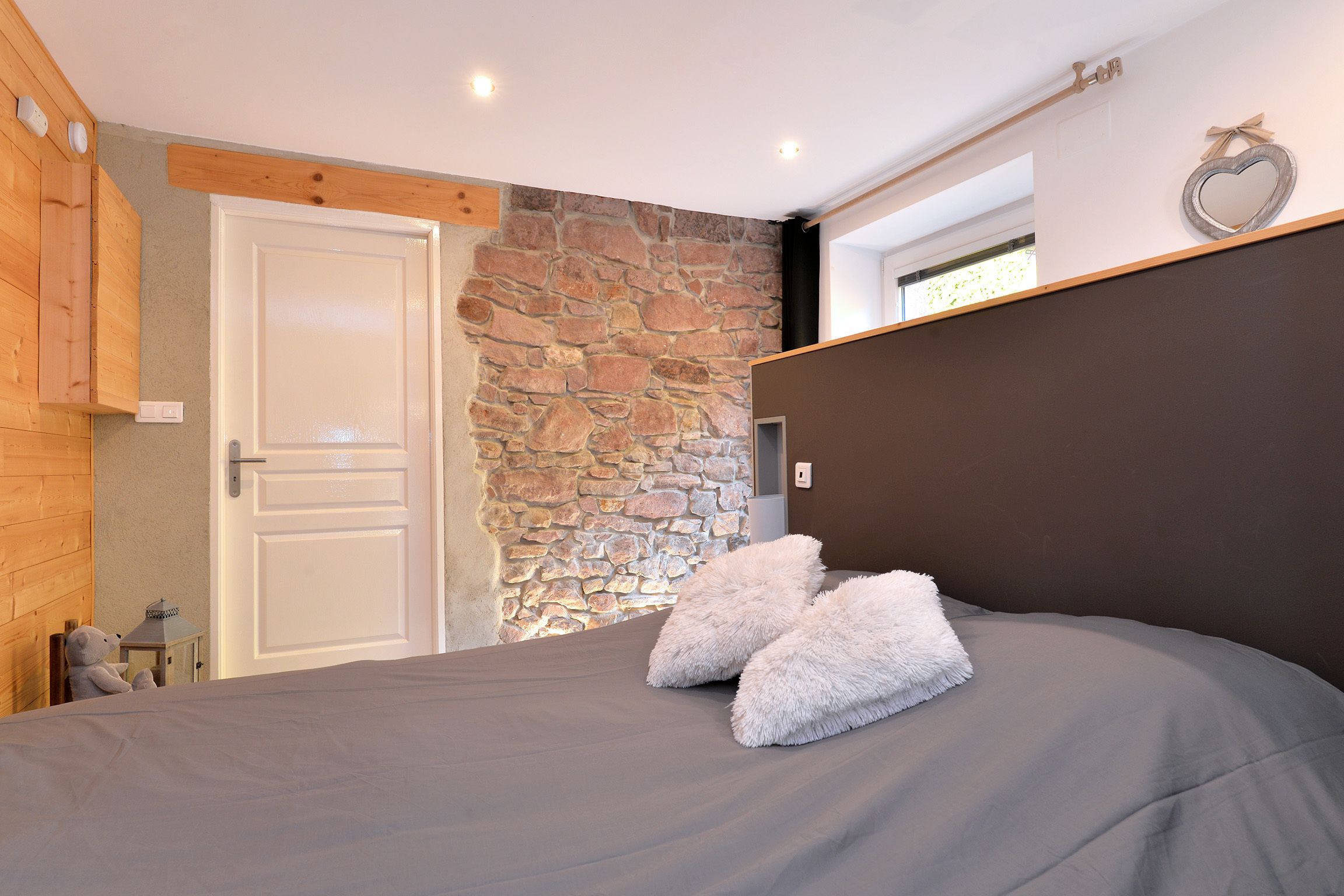 A bedroom with a stone wall, a wooden ceiling, a white door, and a bed with fluffy pillows.