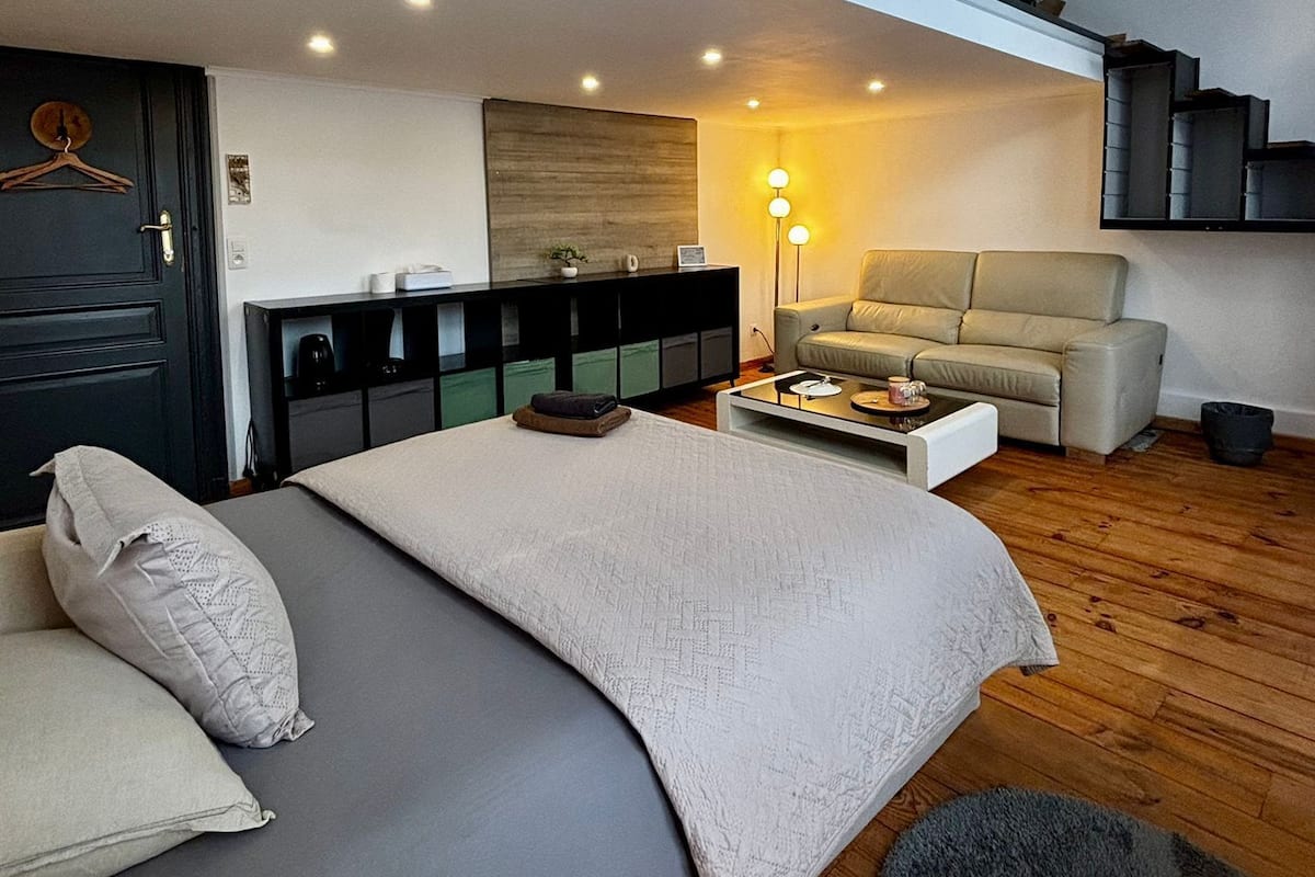 Un dormitorio moderno con una cama grande, un sofá, una mesita de centro y una escalera que lleva a un nivel superior.