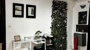 A compact bedroom with a bed, a desk with a chair, a small sink, and a decorative wall with foliage.