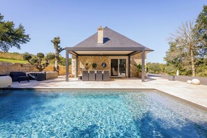 Una casa moderna con piscina, mobiliario exterior y fachada de piedra.