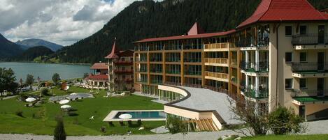 Un hotel con varios balcones, piscina y vistas a un lago y montañas.