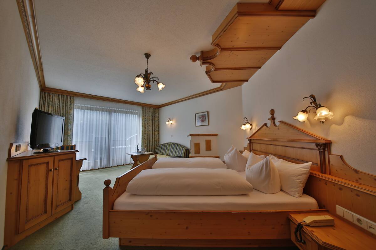 A hotel room with a wooden bed, a television on a wooden cabinet, and a chandelier.