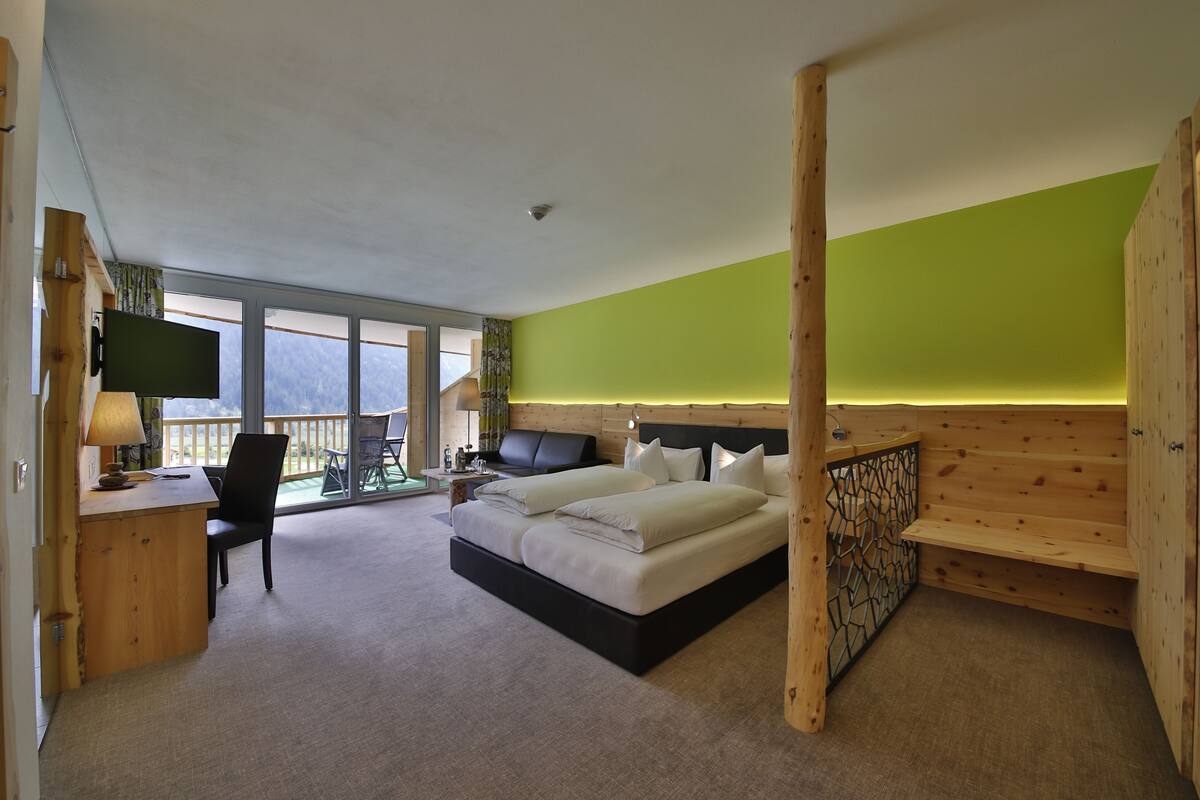 A bedroom with a bed, a desk, a chair, a TV, and a balcony with a view.