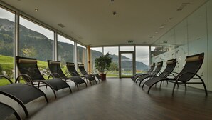 Una habitación con una fila de sillones reclinables frente a grandes ventanales con vistas a un paisaje montañoso.