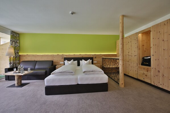 Una habitación de hotel moderna con una cama grande, un armario de madera, un escritorio con lámpara y una pared de acento verde.