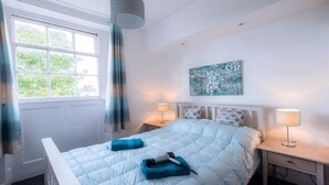 Une chambre à coucher avec un lit, deux lampes de chevet, une fenêtre avec des rideaux et un tableau au mur.
