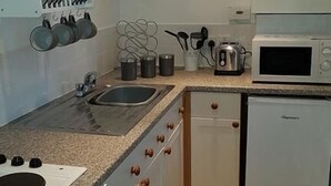 Une cuisine de taille réduite équipée d’un évier, d’une cuisinière, d’un four à micro-ondes et d’un réfrigérateur.