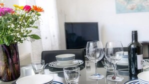Une table à manger dressée avec des assiettes, des verres et une bouteille de vin, et un vase de fleurs placé sur le côté gauche.