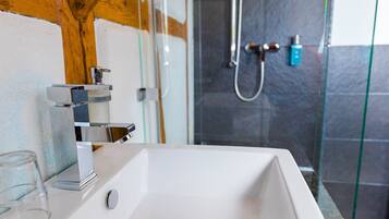 Un baño con lavamanos blanco, cabina de ducha con mampara de vidrio y techo con estructura de madera.