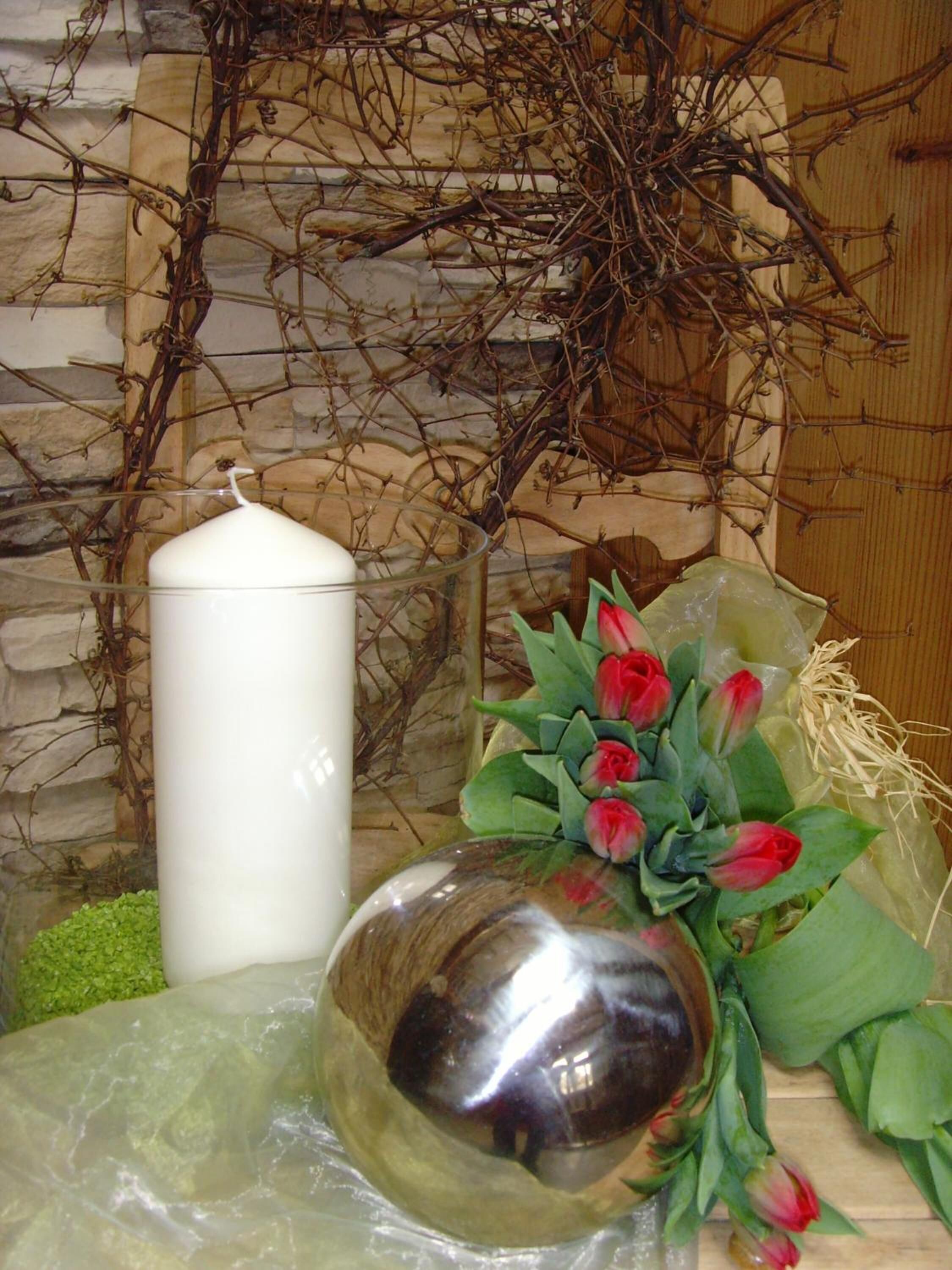A white candle, a metallic vase with red flowers, and a stone wall background.