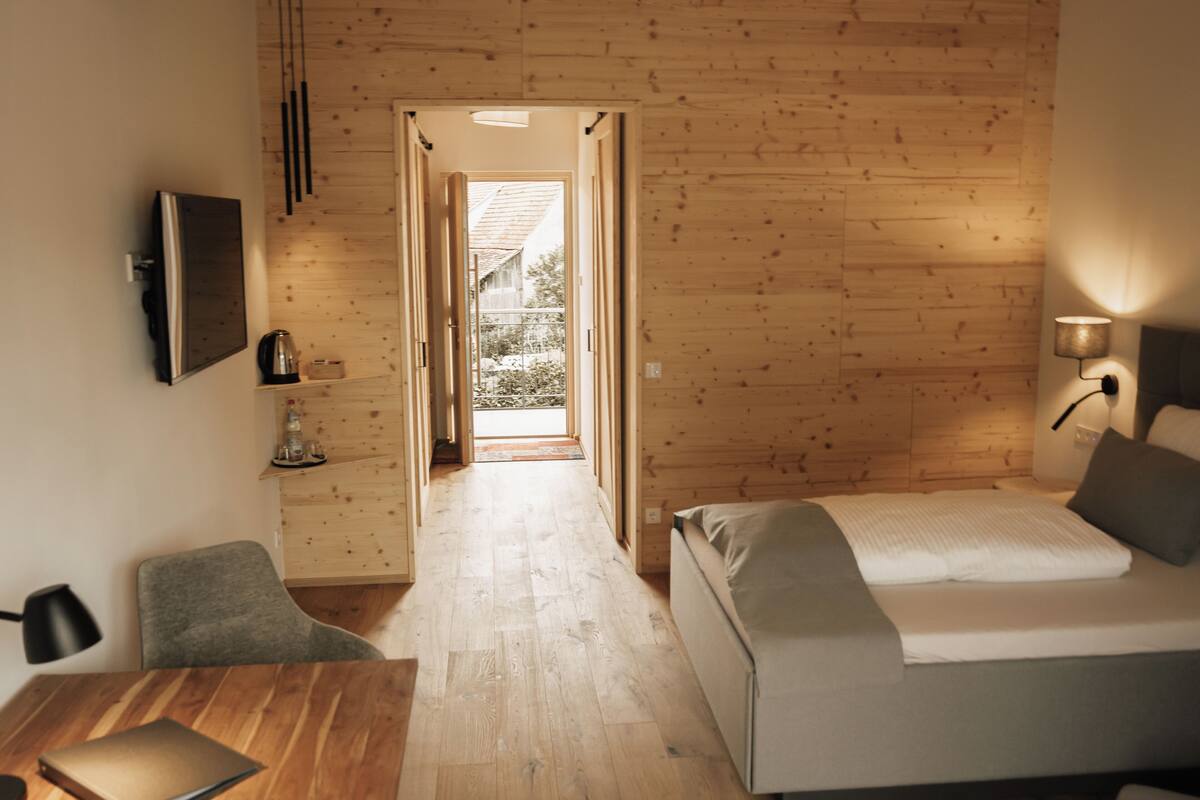 Une pièce comprenant un lit, un bureau et une chaise. Une porte donne accès à un espace extérieur.