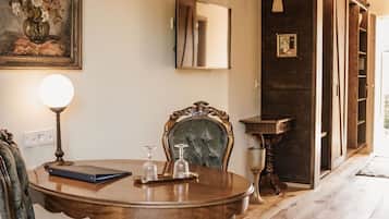 A dining area with a wooden table, two upholstered chairs, a vase of flowers, a lamp, and a mirror on the wall.