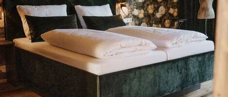 A bedroom with a large bed, dark headboard, floral wallpaper, wooden flooring, and a mannequin in the corner.