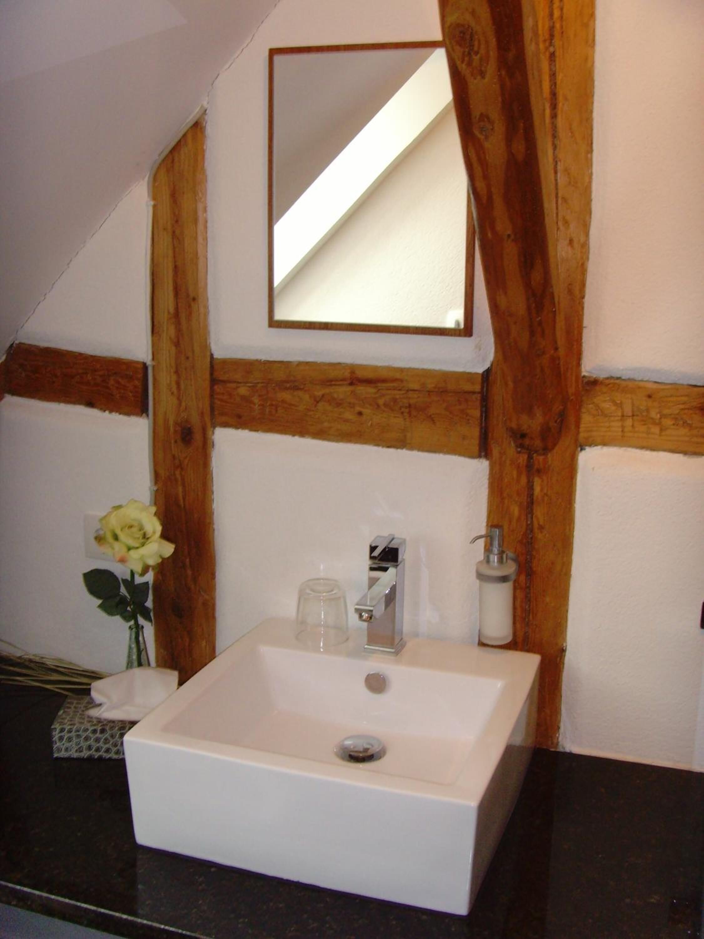 Ein Badezimmer mit weißem Waschbecken, einem Spiegel und Holzbalken.