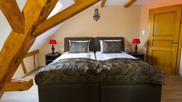 A bedroom with a large bed, two bedside tables with lamps, a wooden door, and exposed wooden beams.