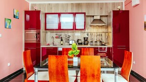 A modern kitchen with red cabinets, a glass dining table, and orange chairs. - Exclusive 3 bedrooms split level sea-views apartment overlooking Bigova Bay (Bigova)