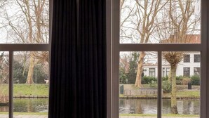 Ein Zimmer mit großem Fenster mit Blick auf einen Kanal, Bäume und ein Gebäude auf der anderen Seite des Wassers.