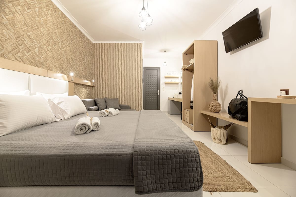 A modern hotel room with a large bed, a TV mounted on the wall, and a wooden wardrobe.