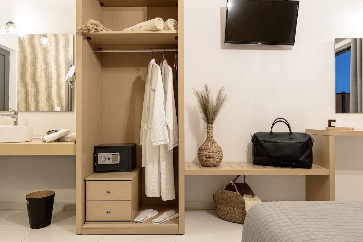 A hotel room with a wooden wardrobe, a flat-screen TV, a mirror, a bedside table with a lamp, and a bed.