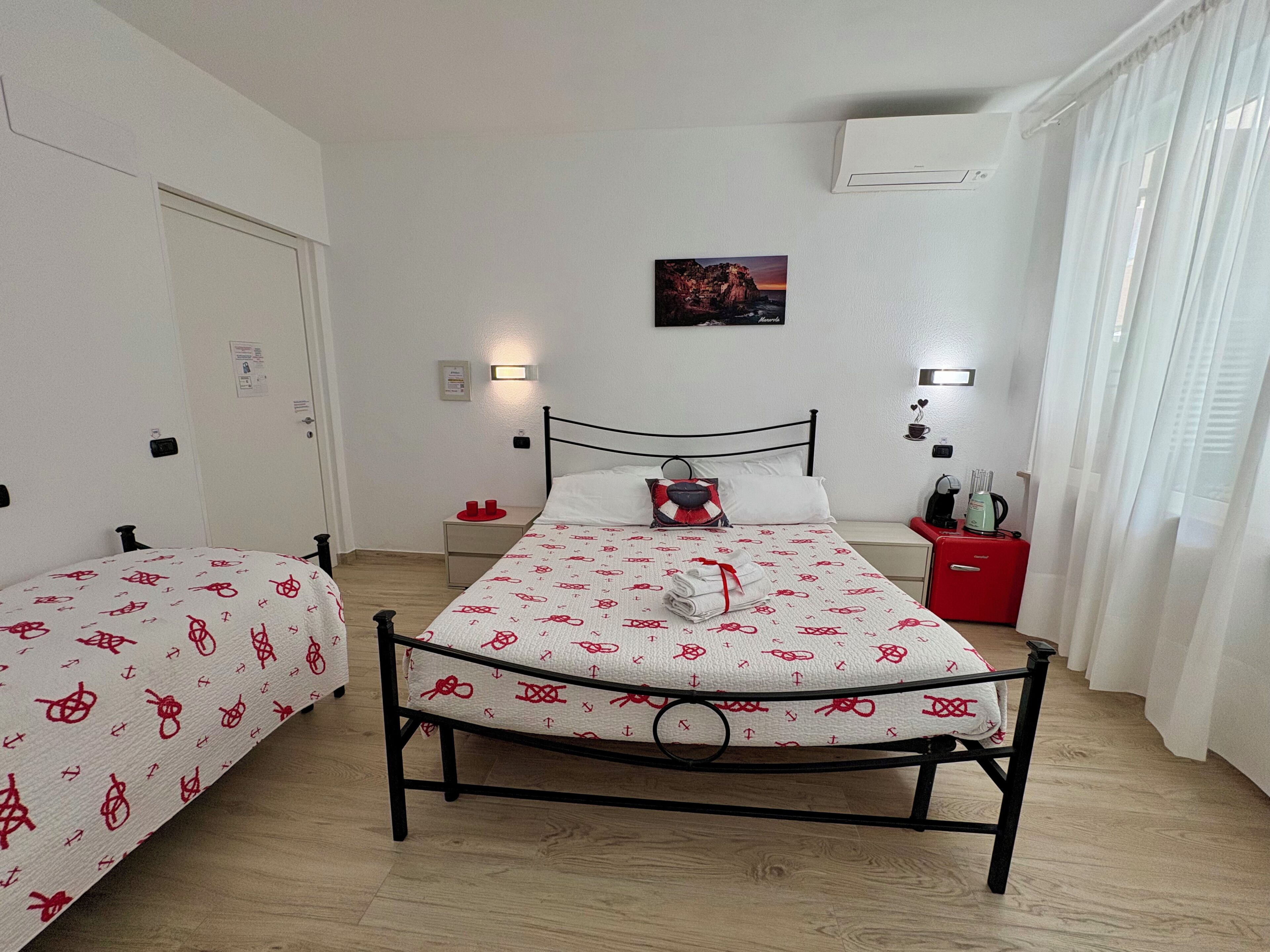 Una habitación con dos camas, una mesita de noche roja, un aire acondicionado instalado en la pared y un cuadro enmarcado.