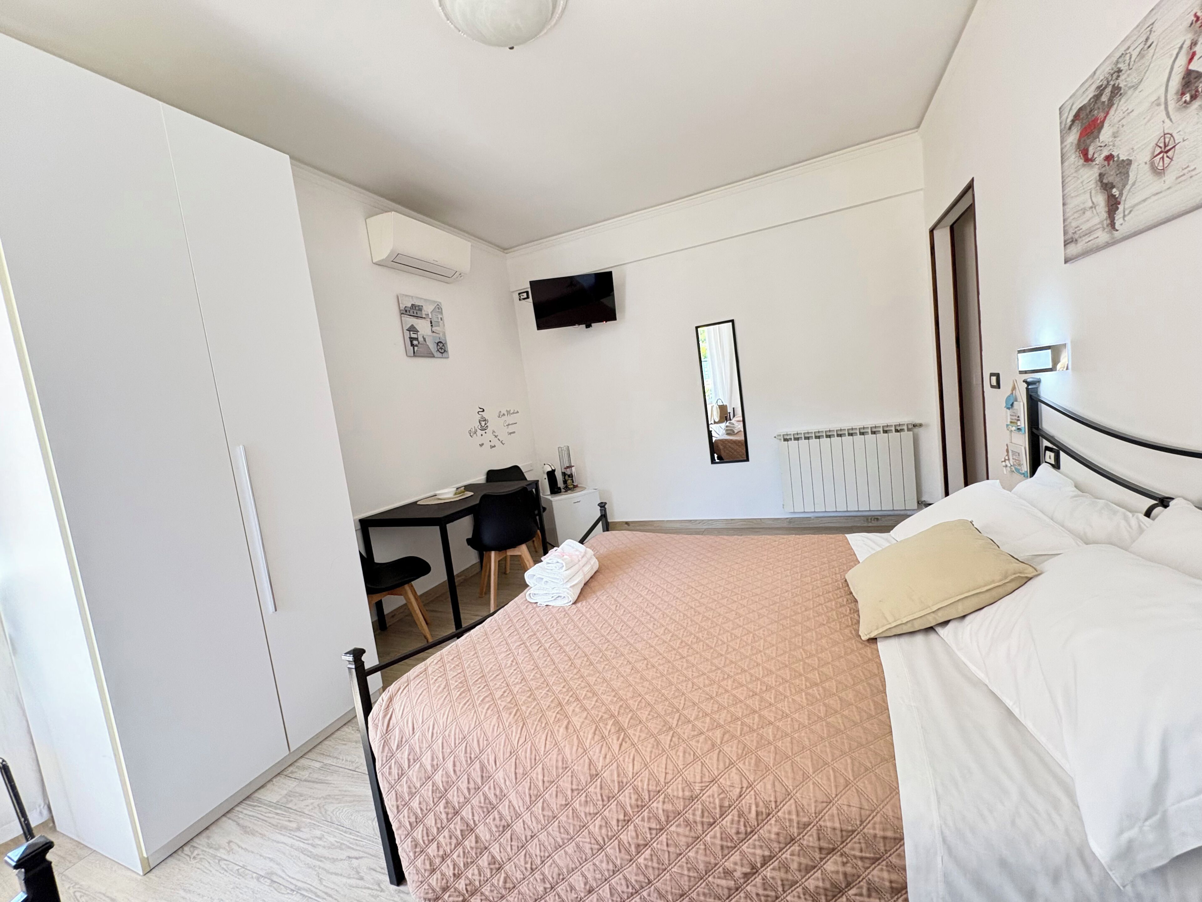 A bedroom with a bed, a desk, a chair, a mirror, and a radiator.