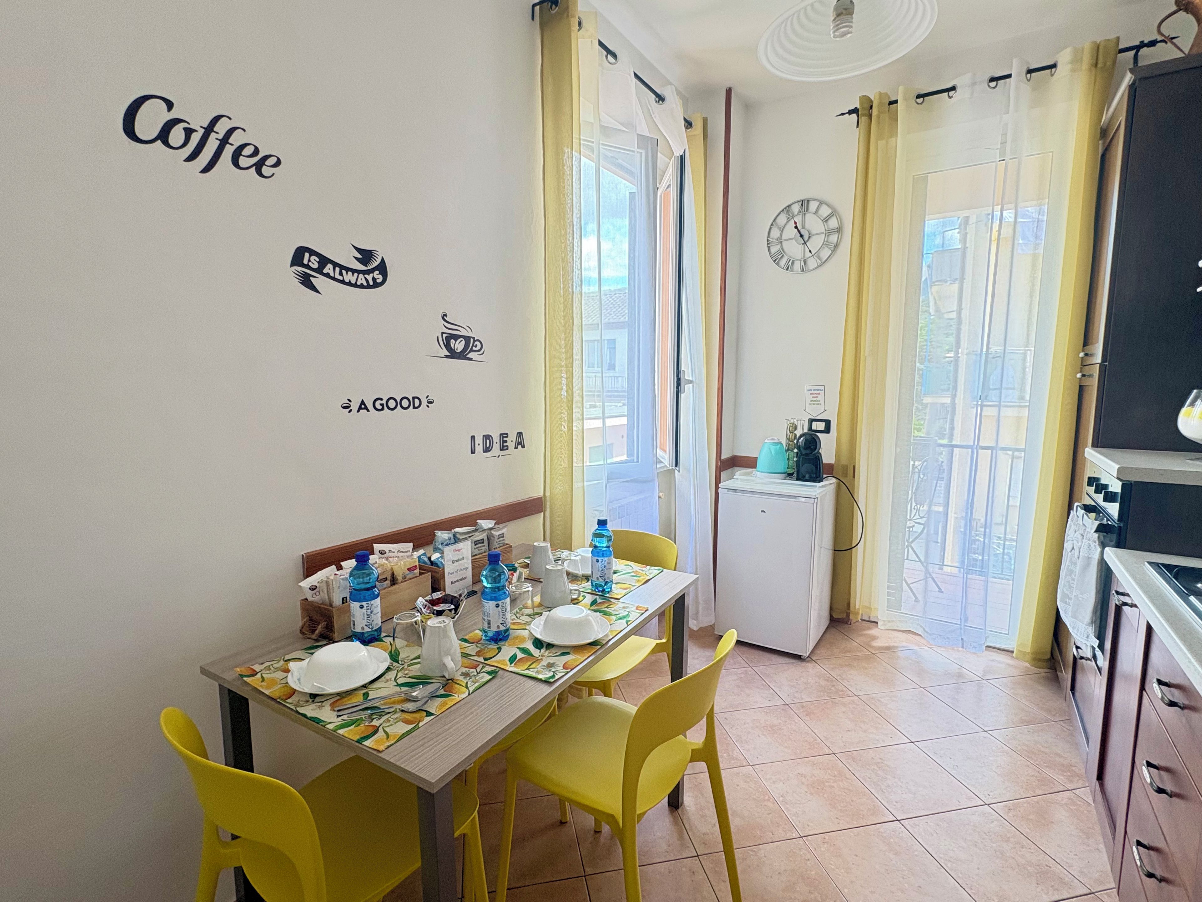 A dining area with a table set for two, a refrigerator, and a clock on the wall.