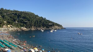 Una playa con hileras de sombrillas y tumbonas, un litoral rocoso y barcos en el agua.
