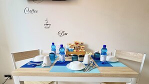 Una mesa de comedor con individuales azules, platos blancos y cubiertos. Hay botellas de agua azules y una jarrón blanco sobre la mesa. Se ve una pequeña señal blanca en la pared que dice 'Coffee' y 'Bar'.