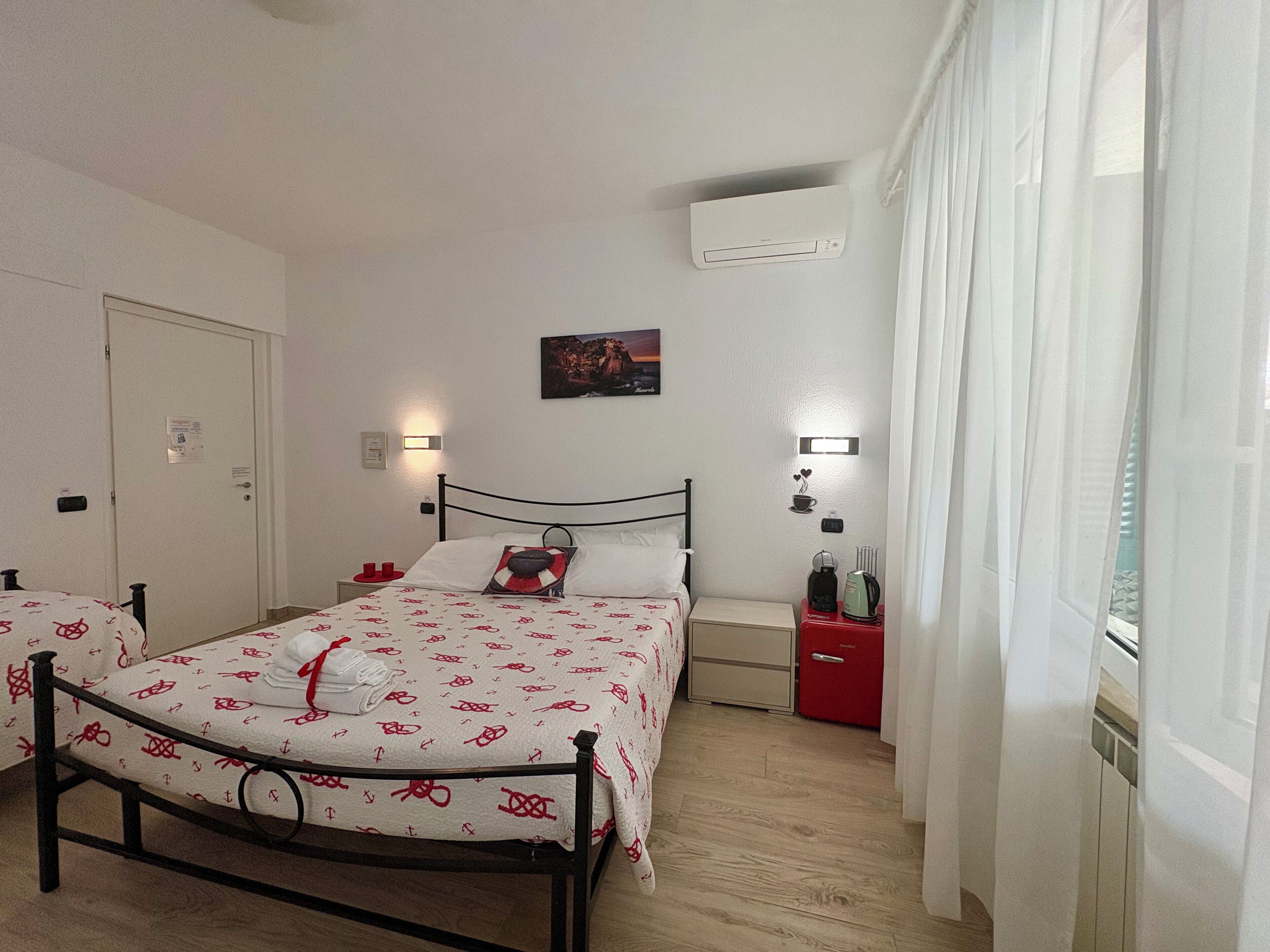 Habitació d'hotel amb llit, taules de nit, aire condicionat, un quadre i una finestra amb cortines.
