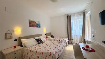 A hotel room with two beds, a dining table, a chair, a small table with a cup, a picture on the wall, and a window with curtains.