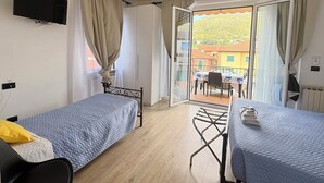 Una habitación con dos camas, televisión, mesa y vistas a un balcón con mesa y sillas.