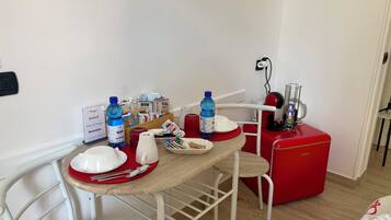 A small dining area with a table set for two, a red refrigerator, and a wall-mounted power outlet.