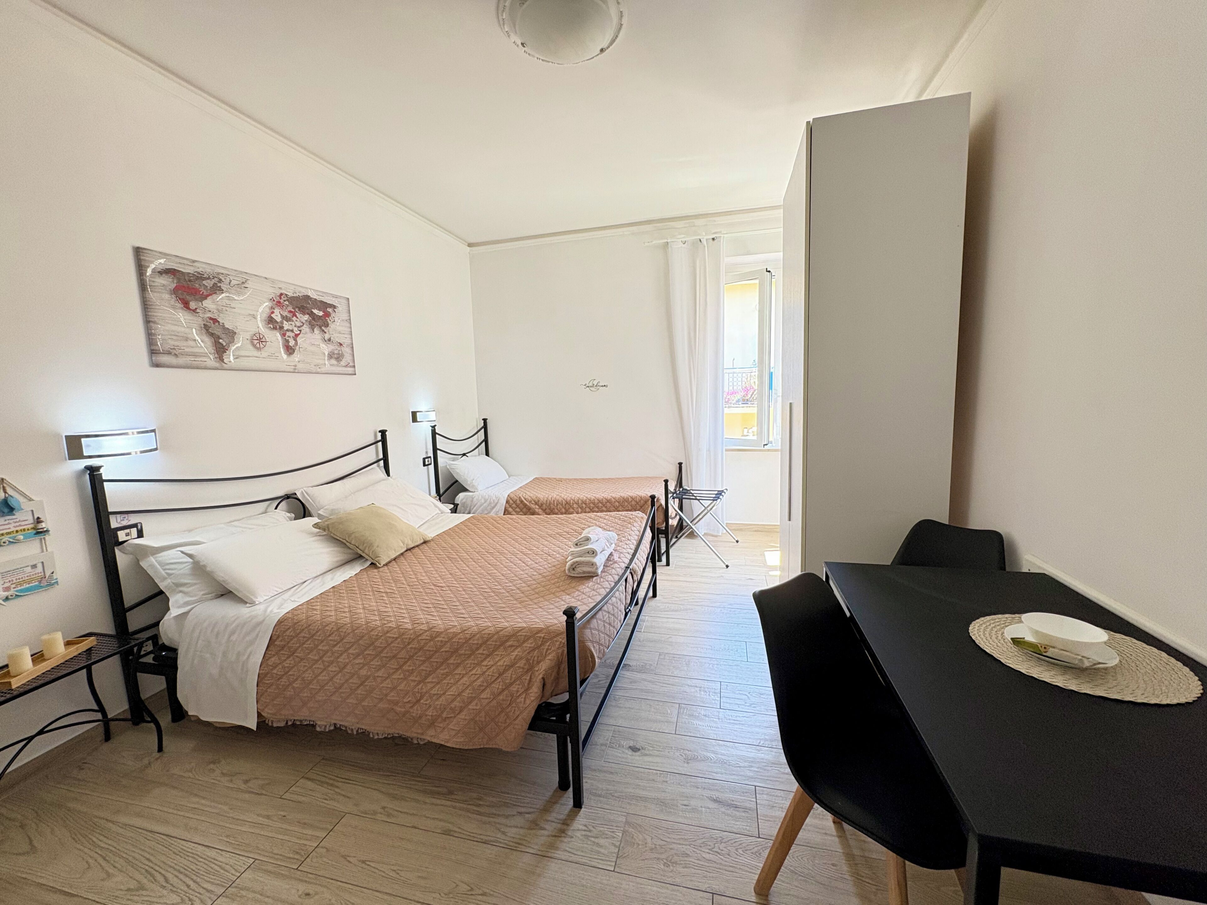 Een slaapkamer met twee bedden, een bureau, een stoel, een kaart als kunstwerk, en een raam met gordijnen.