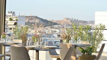 A rooftop dining area with tables set for two, overlooking a cityscape with historical buildings and a hill.