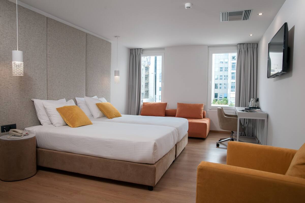 A modern hotel room with a large bed, a desk, a chair, and a TV.