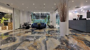 A modern hotel lobby with a marble floor, seating area, reception desk, and large windows. - Athenaeum Smart Hotel (Athens)