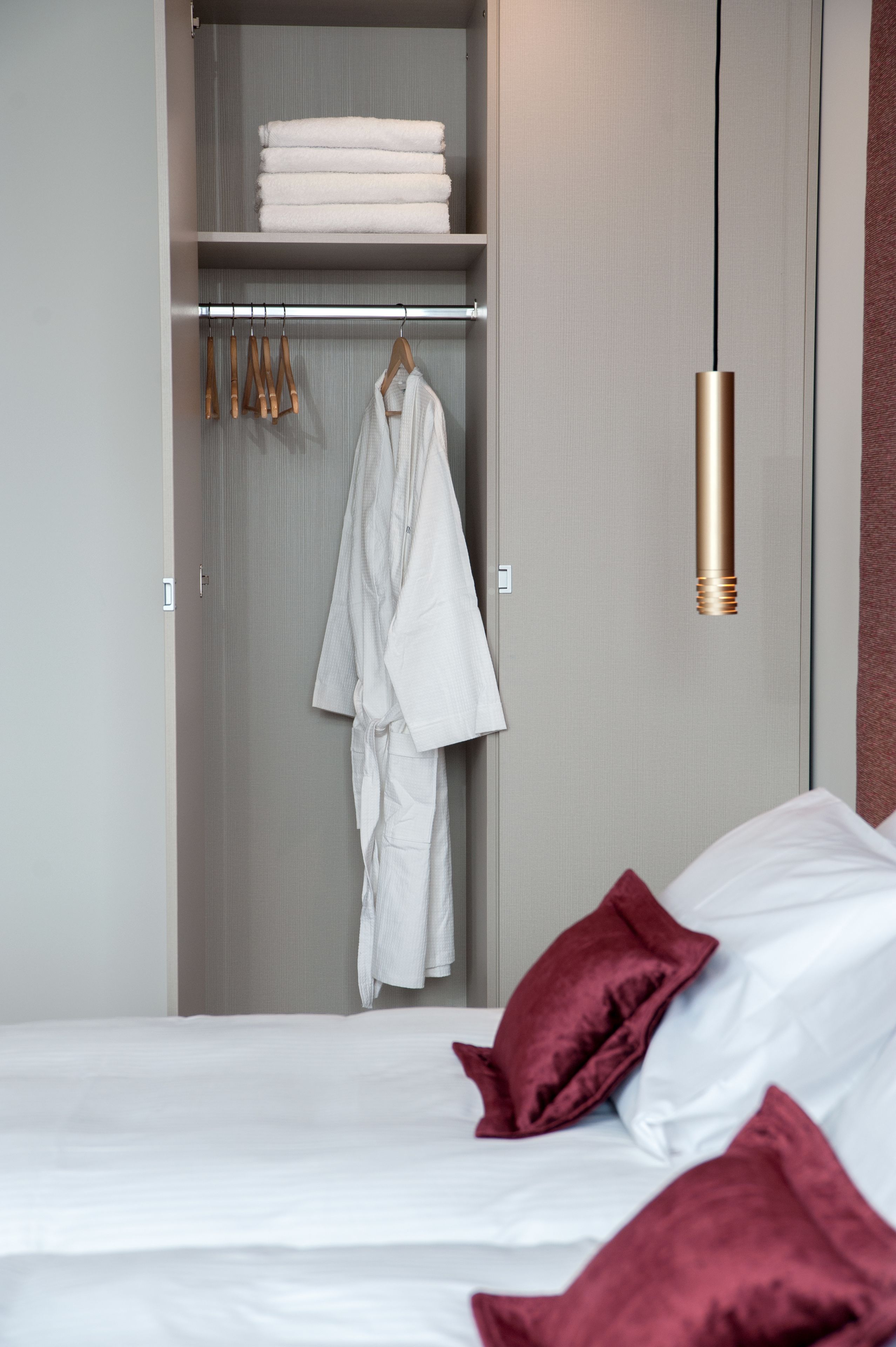 A bedroom with a bed, a closet with hanging clothes, and a robe hanging on a rack.