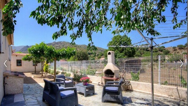 An outdoor patio with wicker furniture, a stone floor, and a wood-fired oven. - Gîte Calzolari in Corsica (Castifao)