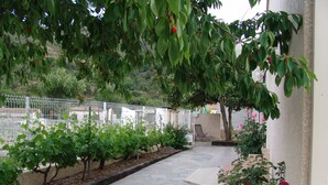 A stone pathway leading to a seating area with a view of a fenced garden and a hill in the background. - Gîte Calzolari in Corsica (Castifao)